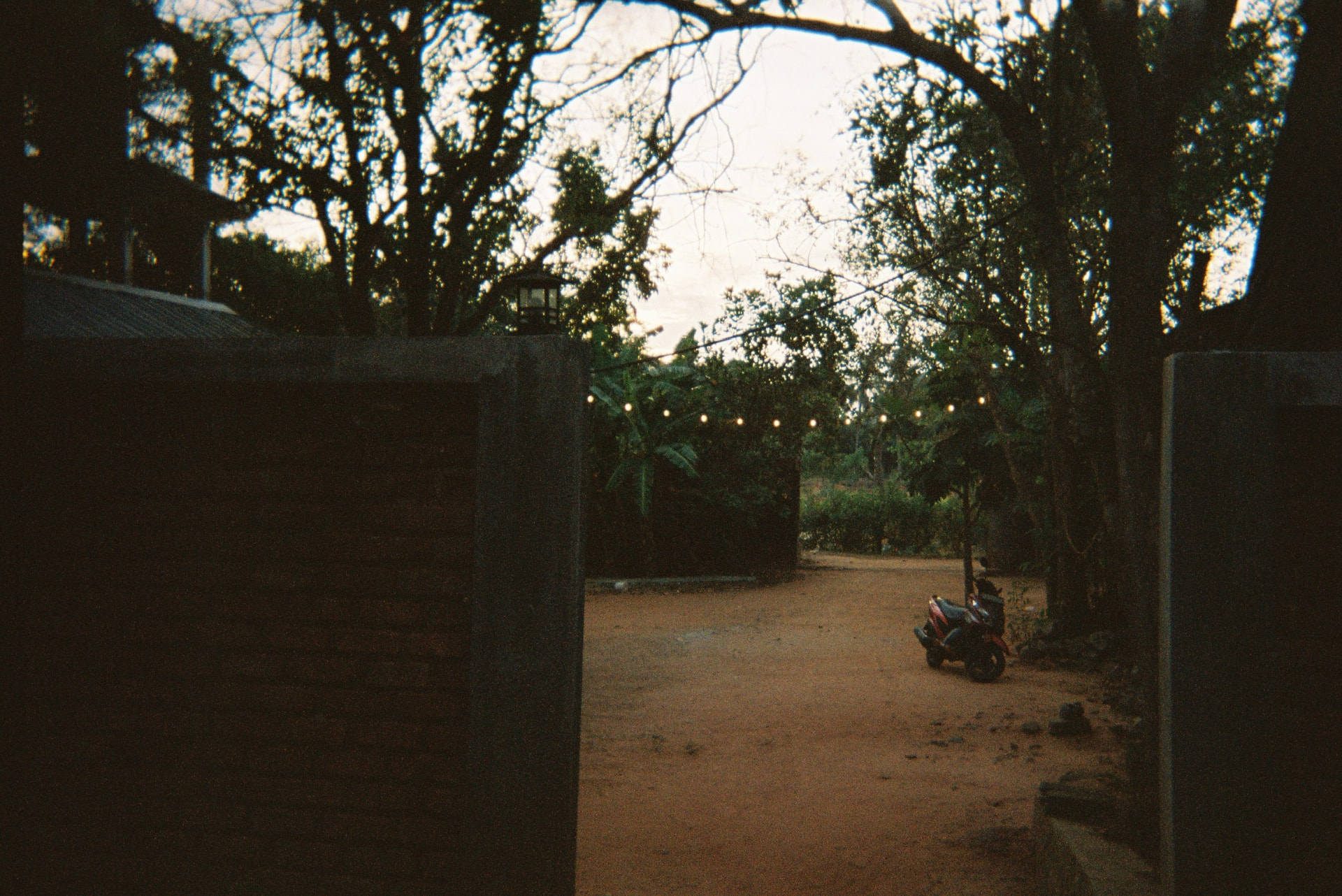Red dirt courtyard at dusk with a scooter under string lights