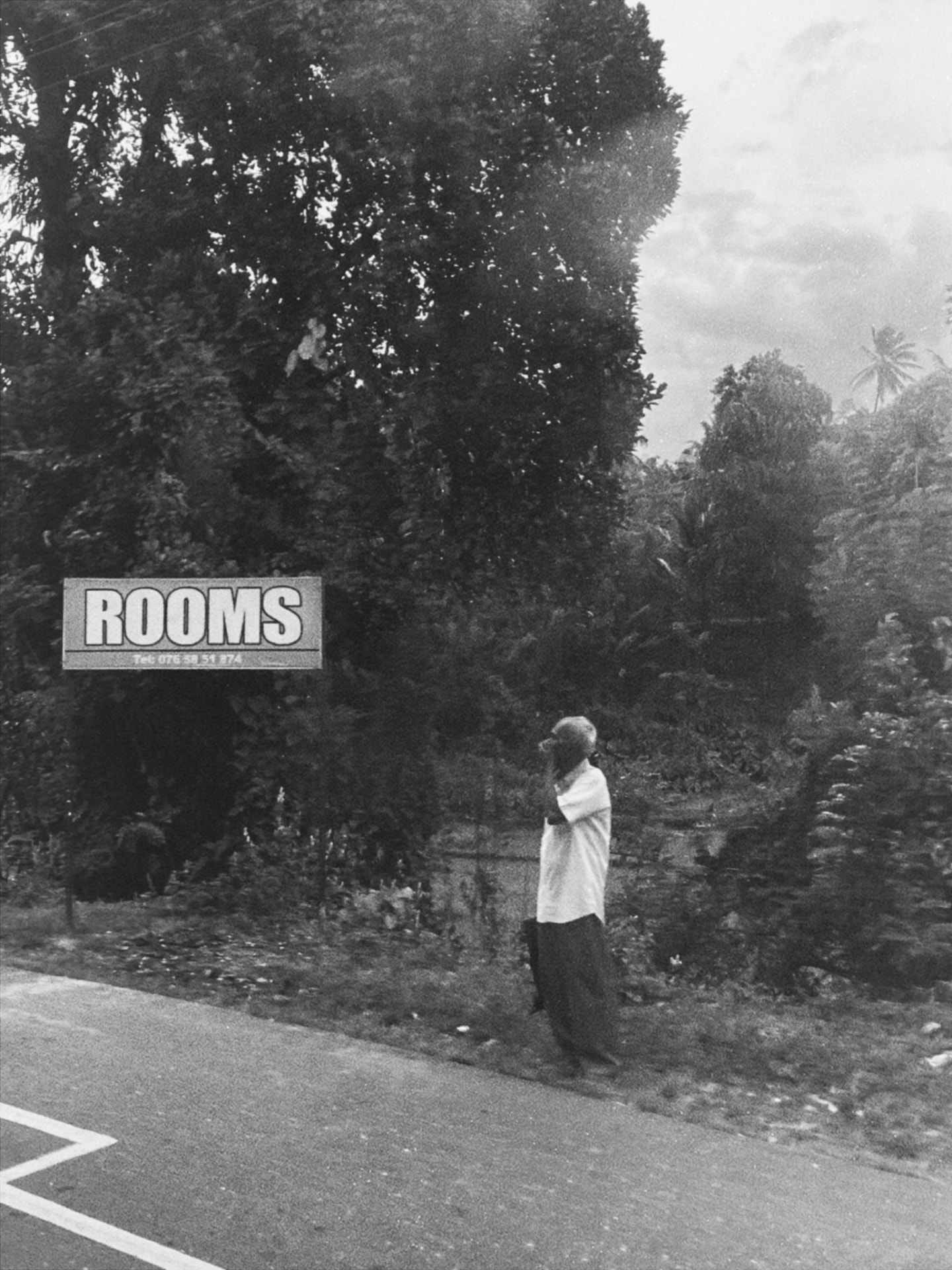 Man standing under a roadside sign reading ROOMS