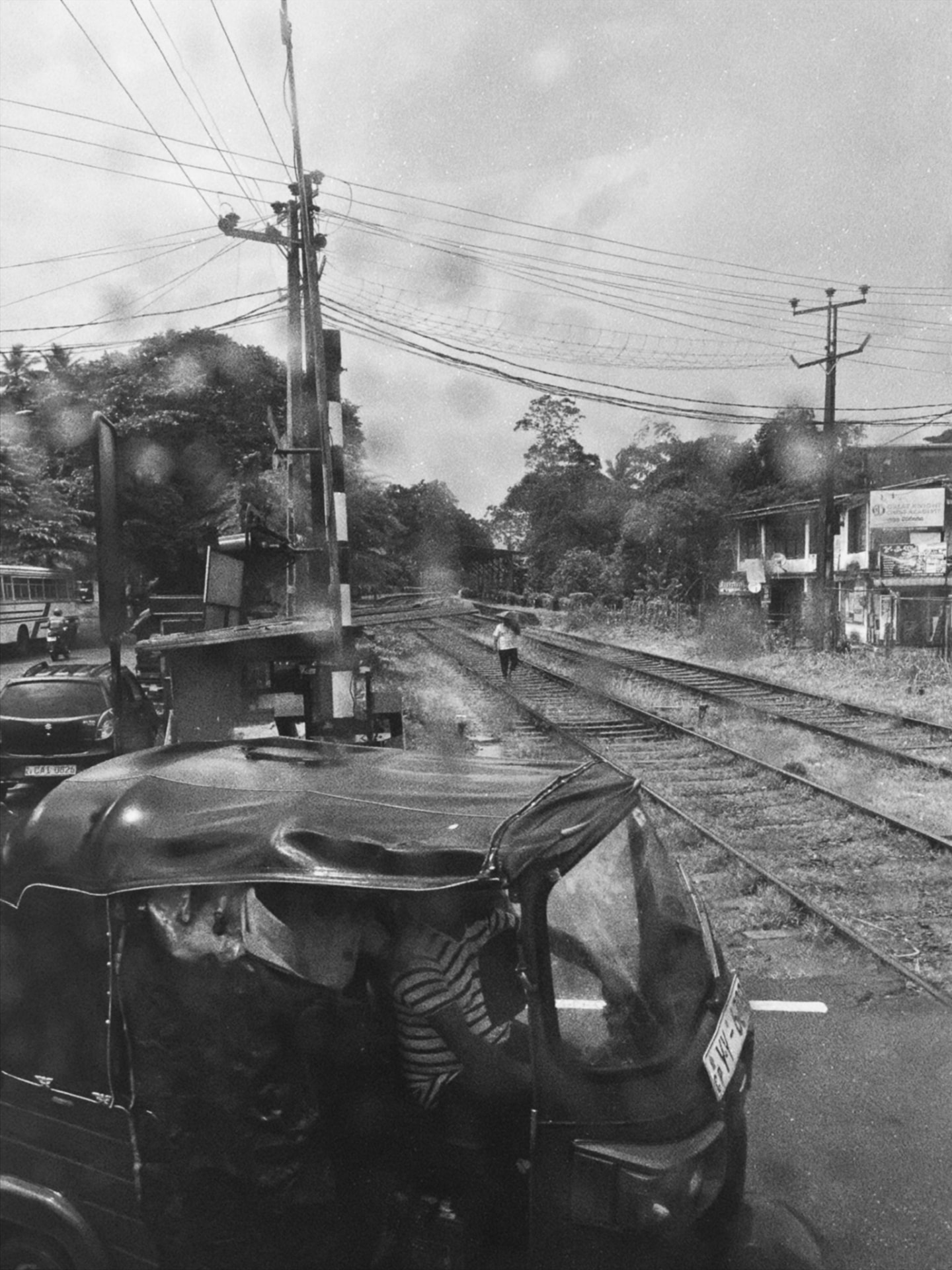 Tuk-tuk waiting at a railway crossing with a figure walking the tracks