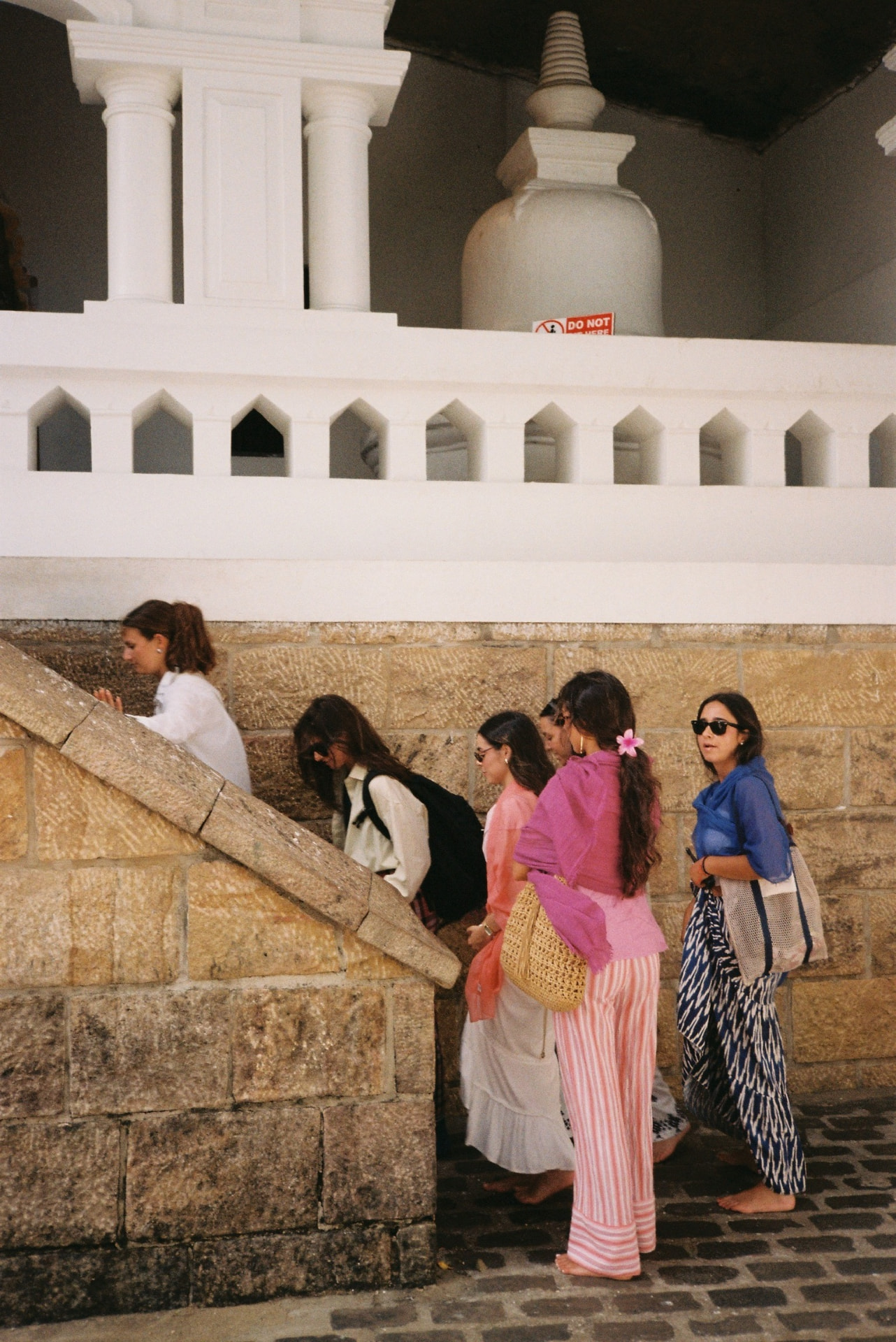 Barefoot visitors walking along the white wall of a stupa