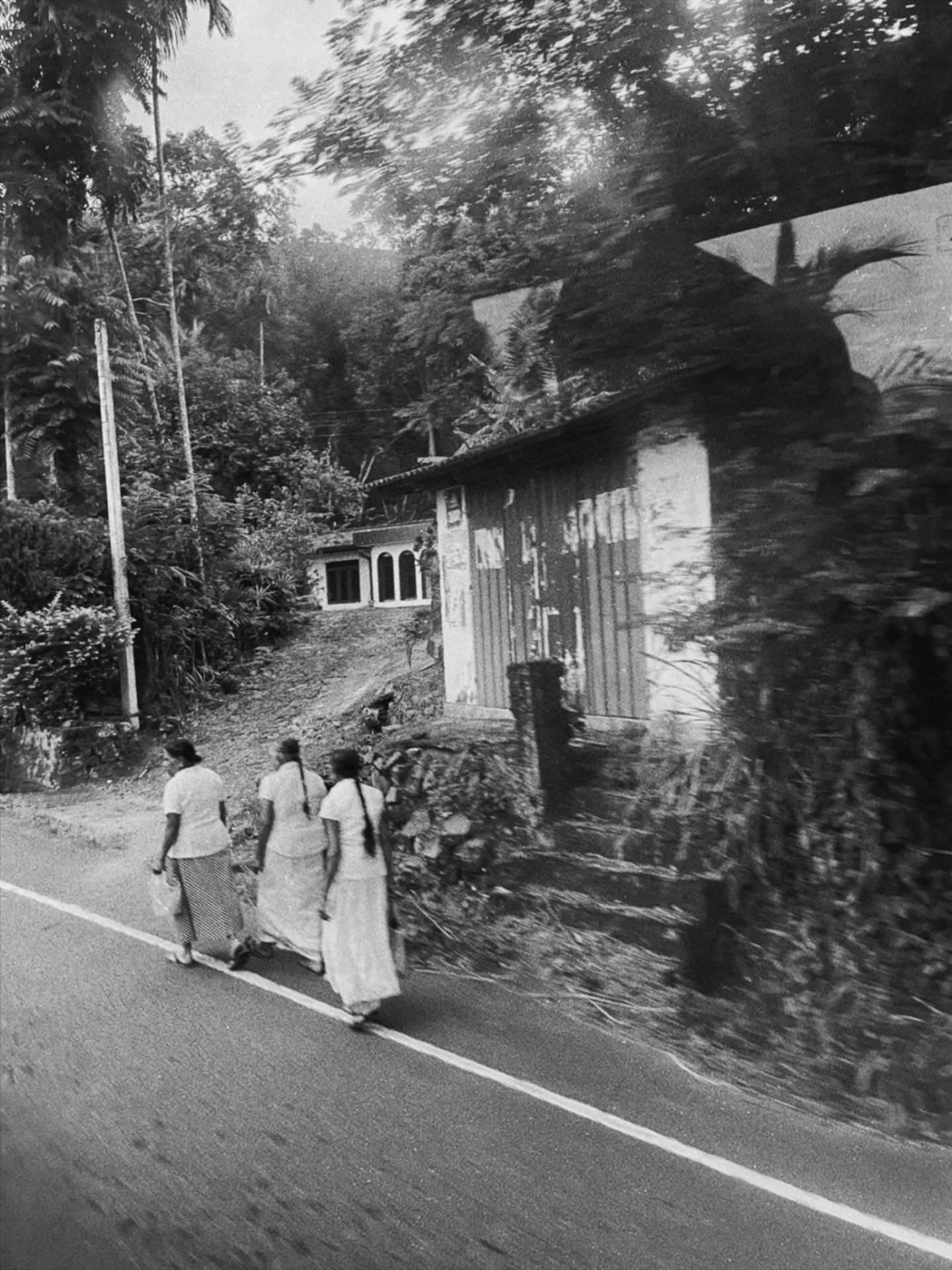 Three women in white walking along a road, motion blurred