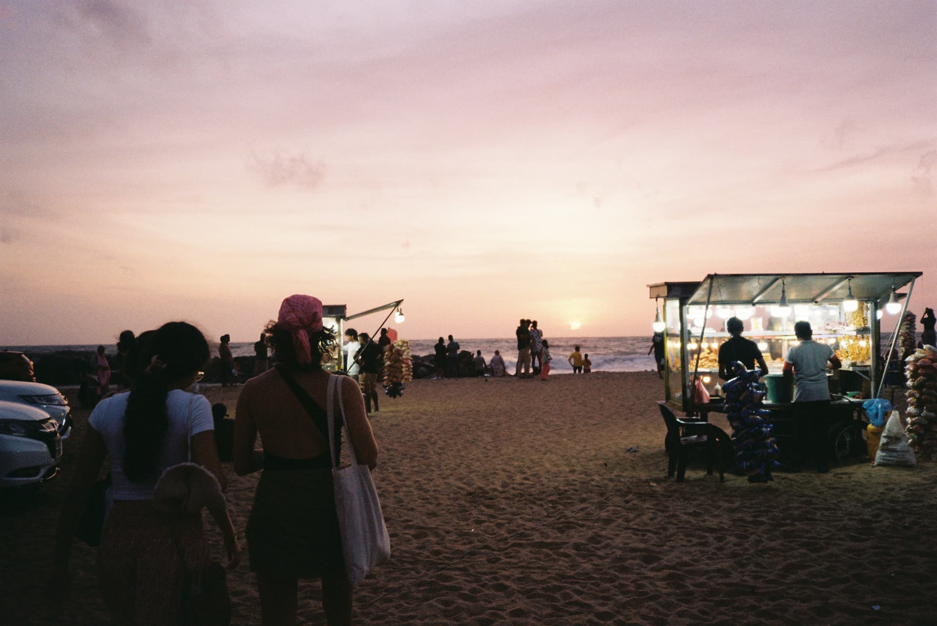 Silhouetted figures walking past glowing food stalls at sunset