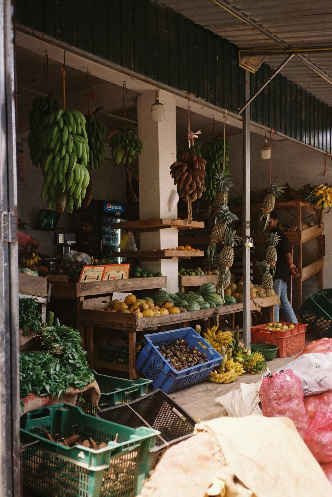 Fruit and vegetable market stall with hanging bananas and pineapples